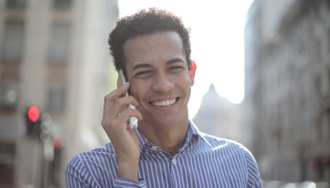 Un hombre con cabello castaño y una camisa a rayas azules que sonríe mientras habla por teléfono.